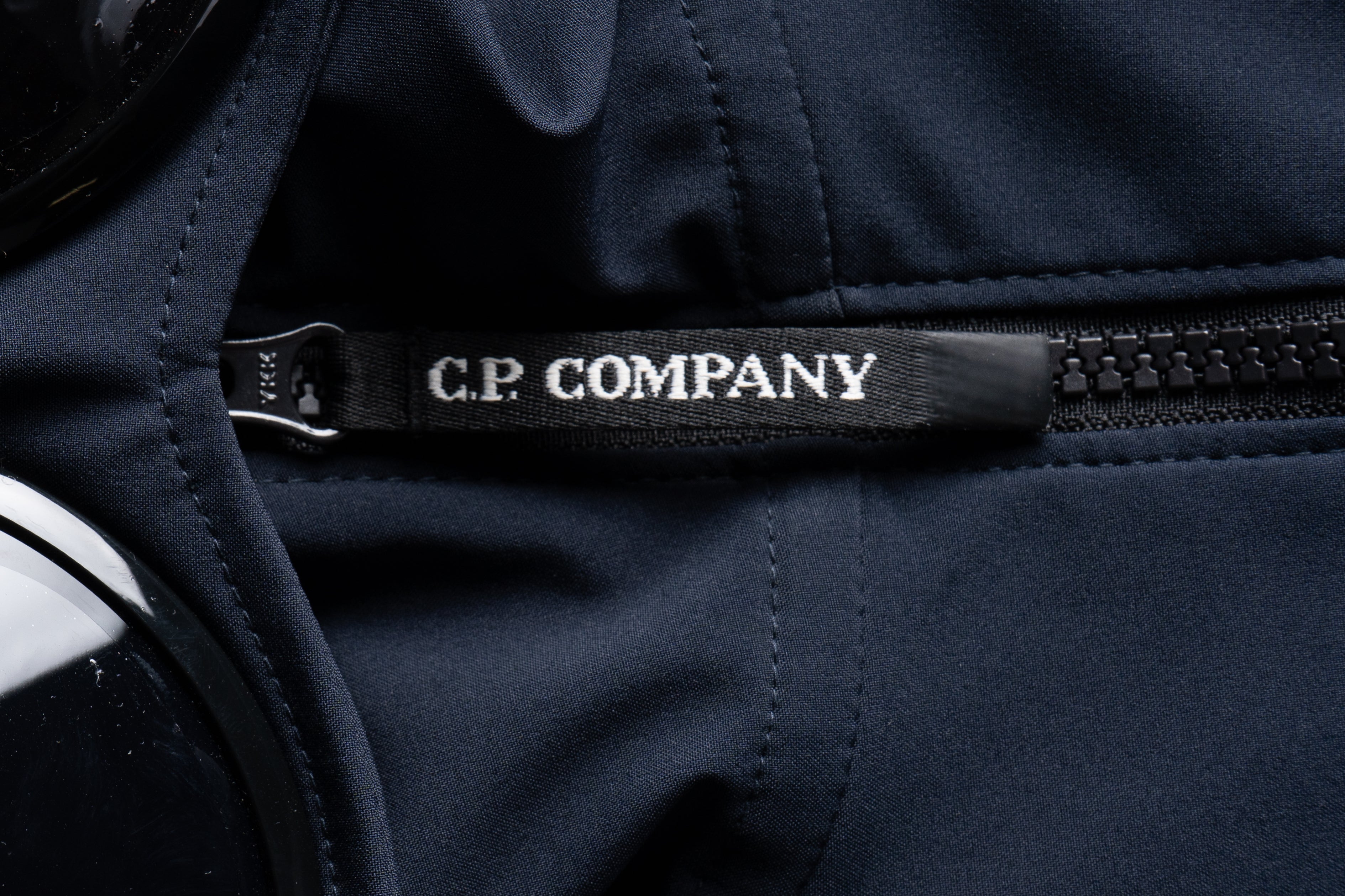 Étiquette de la Veste CP Company Bleu Marine, mettant en avant le logo distinctif sur le tissu.