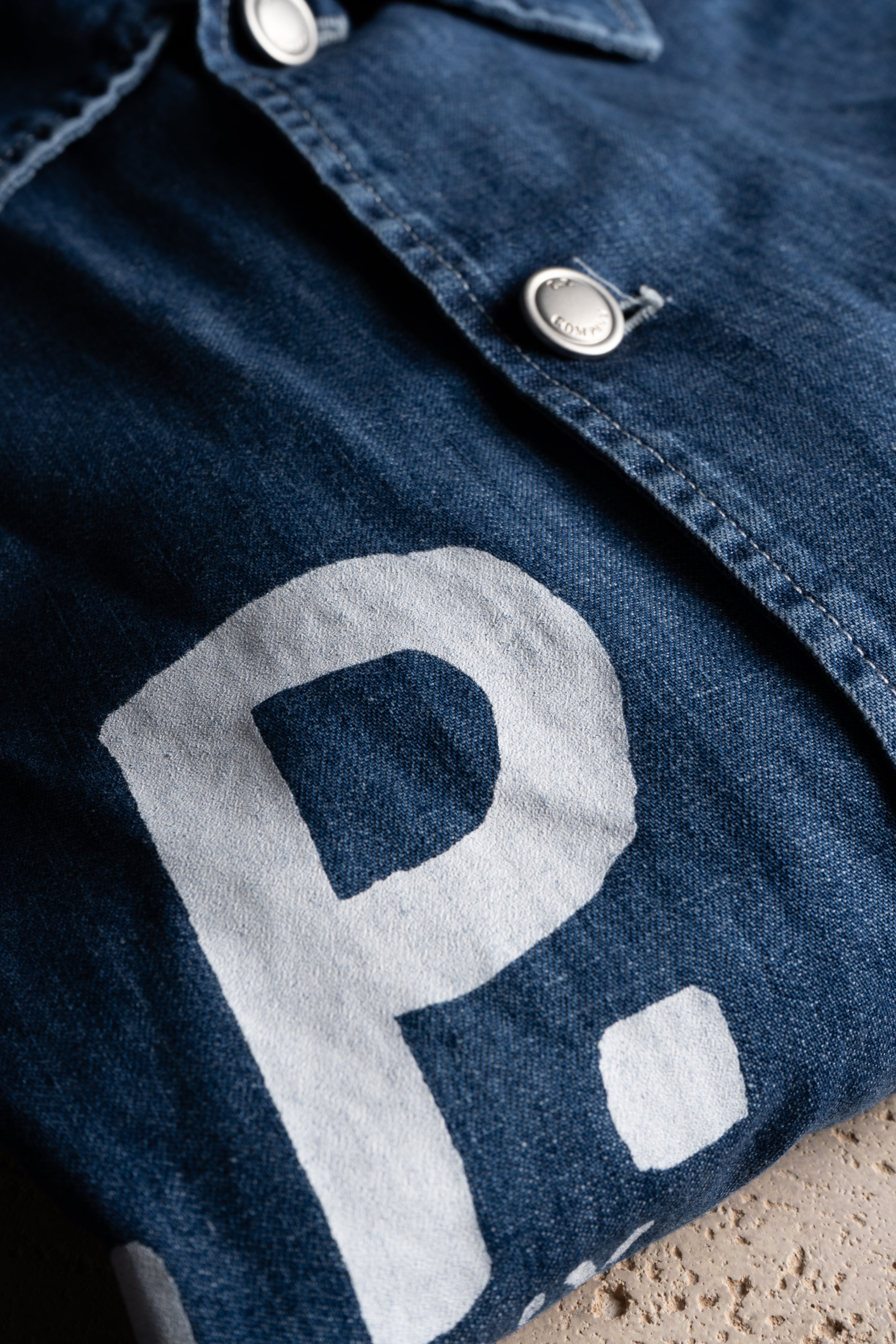 Detail of CP Company blue denim jacket showcasing the logo and high-quality fabric.